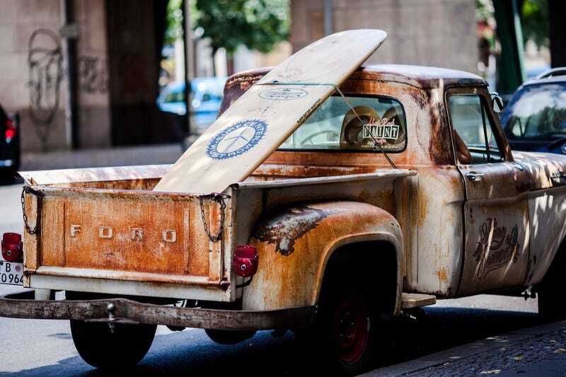 An old rusty pickup truck with a surfing board in the cargo bed
